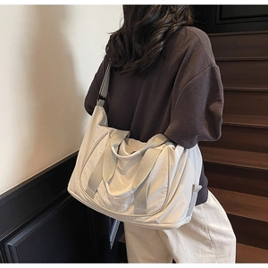 Détail d'un grand sac de voyage en nylon blanc cassé porté par une personne en situation