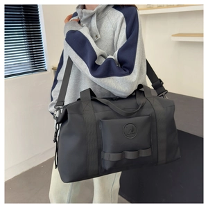 On-body view of a large black travel duffel bag with shoulder strap and front zipper pocket
