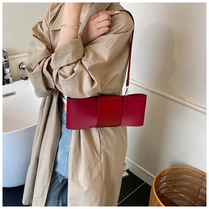 Detail of red bow-shaped leather shoulder bag with slim strap on cream background