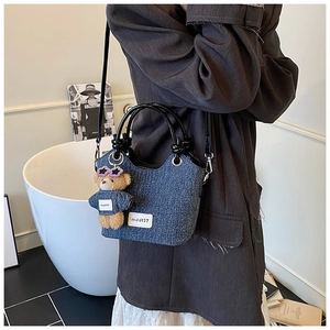 Détail du sac seau en denim avec poignées rondes et breloque ours en peluche mignonne