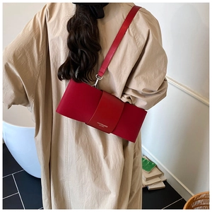 Close-up of red matte leather shoulder bag with flap and fashion logo on beige trench coat
