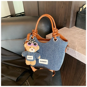 Détail du sac seau en denim avec poignées en cuir, bord ondulé et breloque ours