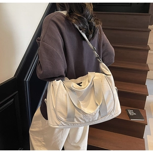Détail d'un grand sac de voyage crème avec de larges bandoulières sur un escalier en bois