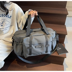 Détail du sac de voyage gris avec poignées renforcées et poche avant sur un escalier