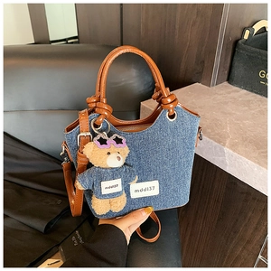 Détail du sac seau en denim avec lanières en cuir marron et pendentif ours peluche