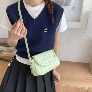 Close-up of light green checkered crossbody bag worn by model in a cozy home setting