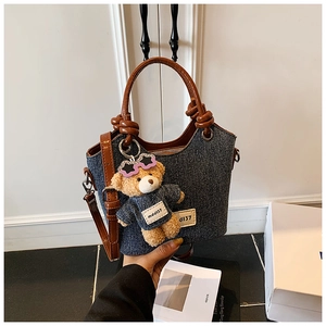 Détail du sac seau en denim avec sangle en cuir et breloque ours en peluche et lunettes