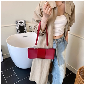 Close-up of stylish red leather bow shoulder bag for women held by a model
