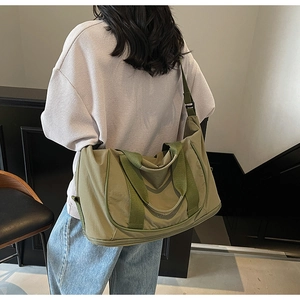 Vue détaillée du grand sac de voyage vert olive porté par un mannequin dans une pièce