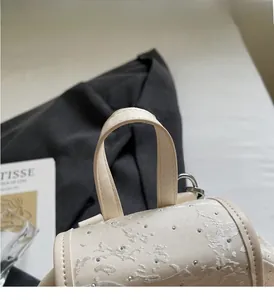 Macro detail of beige backpack featuring floral embroidery, silver studs and sturdy leather handle