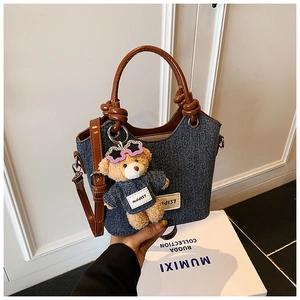 Détail du sac seau en jean montrant la bandoulière en cuir brun et le charme d'ours