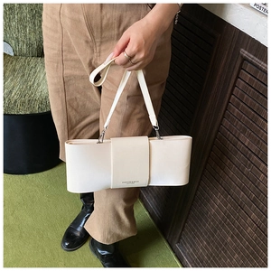 Detail of minimalist white rectangle leather bag featuring a bow-like fold and strap