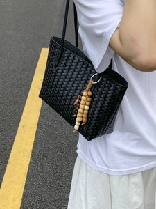 Black woven leather tote bag for women with wooden bead tassel in a casual outdoor setting