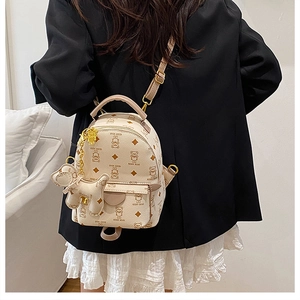 Close-up of beige mini backpack with teddy bear prints and cute dog charm on model