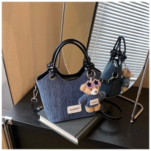 Vue détaillée du sac seau en denim avec poignées noires brillantes et charm d'ours