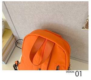 Detail of orange nylon backpack showing top handle, dual zippers and black metal hardware
