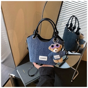 Gros plan d'un sac cabas en jean avec poignées en cuir et breloque ours en peluche