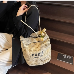 Détail du sac fourre-tout en paille tissée beige avec texte PARIS sur escalier bois