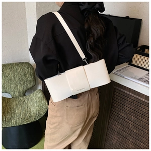 Close-up of a white bow-shaped leather underarm bag worn by a model in a cozy interior