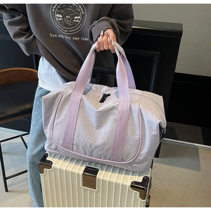 Détail du grand sac de voyage lilas avec poignées renforcées sur une valise blanche