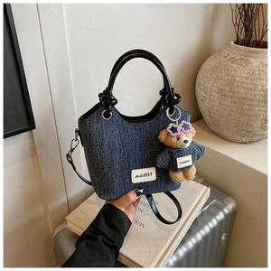 Détail du sac seau en denim avec poignée en cuir nouée et charm ours en peluche