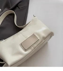 Detail of soft cream-colored underarm bag with rectangular metal plate and wide strap