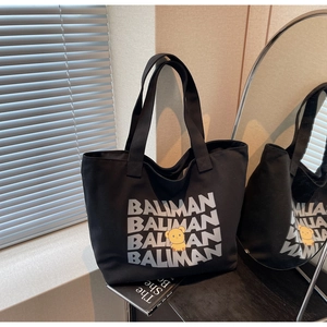 Detail of a black canvas tote bag featuring BALIMAN text and a yellow cartoon bear motif