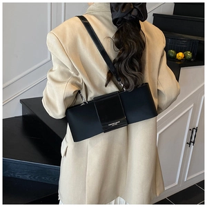 Detail of minimalist black leather underarm bag with decorative branded buckle strap