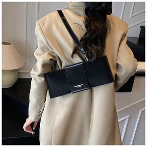 Detailed back view of a minimalist black leather underarm bag on a model in a beige blazer