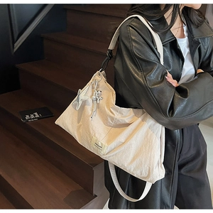 Detail of beige nylon tote bag with star pendant and knotted shoulder strap detail