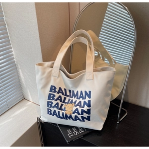 Detail of white canvas tote bag with blue Baliman lettering and yellow bear illustration