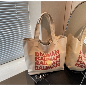 Detail of beige canvas tote bag with red BALIMAN text and cute yellow bear graphic