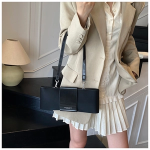 Detail of minimalist black leather shoulder bag styled with a beige suit and pleated skirt
