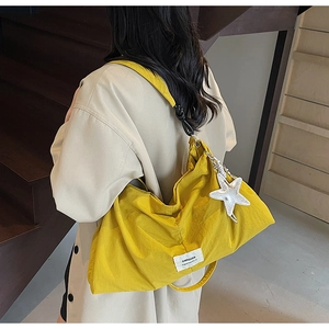 Close-up of bright yellow canvas tote bag with star pendant and woven label on a model