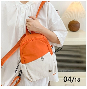 Detail of a mini two-tone nylon backpack in orange and beige worn as a crossbody bag