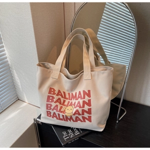 Detail of cream canvas tote bag featuring a red BALIMAN logo and cute cartoon bear print