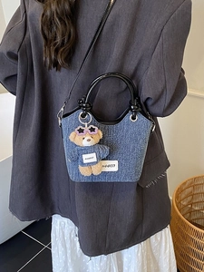Sac seau en denim bleu avec anses noires et pendentif ours porté par un mannequin