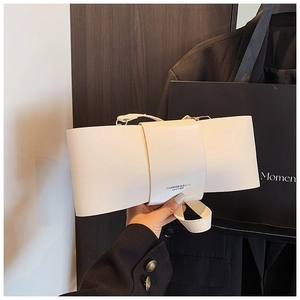 Detail of a creamy white bow-shaped shoulder bag featuring a gold fashion logo engraving
