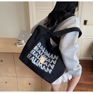 Detail of black canvas tote bag featuring repeated lettering and a yellow cartoon bear