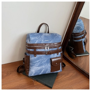 Detailed close-up of blue denim backpack with brown leather trim and side pocket view