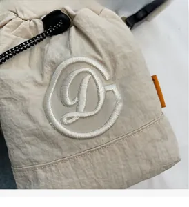 Detail of beige drawstring crossbody bag with large floral embroidered letter D and striped cords