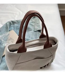 Detailed close-up of beige canvas tote bag with brown straps and embroidery detail