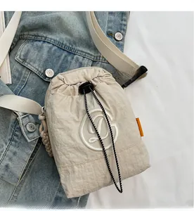 Detail of beige nylon drawstring crossbody phone bag with white embroidery and orange tag
