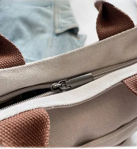 Detail of smooth metal zipper closure on a beige canvas tote bag with brown straps