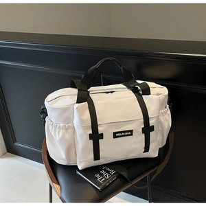 Détail du grand sac de voyage blanc avec sangles noires sur une chaise en cuir