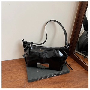 Detail of black patent leather tote bag with silver metal zipper and rectangular metal plate