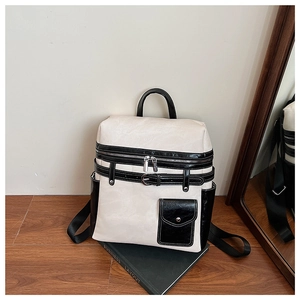 Detail of a cream and black two-tone backpack with metal zippers and decorative straps