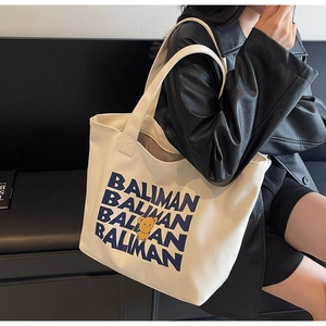 Close-up of white canvas tote with blue BALIMAN text and yellow bear on black background