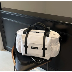 Détail d'un sac de voyage blanc avec poignées noires et étiquette tissée sur une chaise