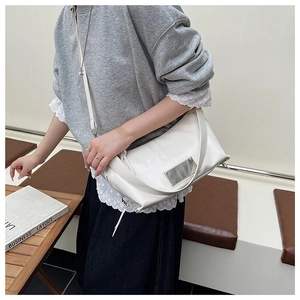 Detailed view of white leather tote bag with silver metal plaque and sleek zipper closure